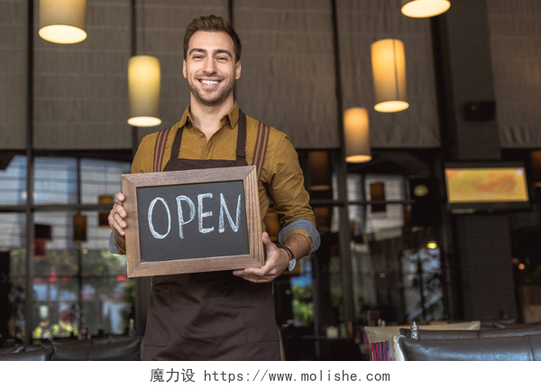 咖啡厅的咖啡师在店内微笑的欢迎顾客有吸引力的微笑侍者举行黑板与开放铭文在咖啡厅